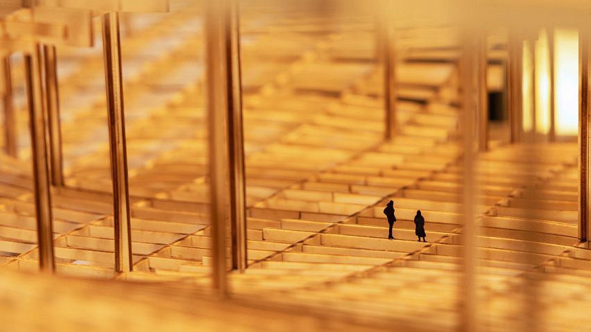Photo of an architecture exhibit at the 2023 ECC Architecture Biennale. Close-up of a wooden structure with small shadow cut-outs of people in the model.